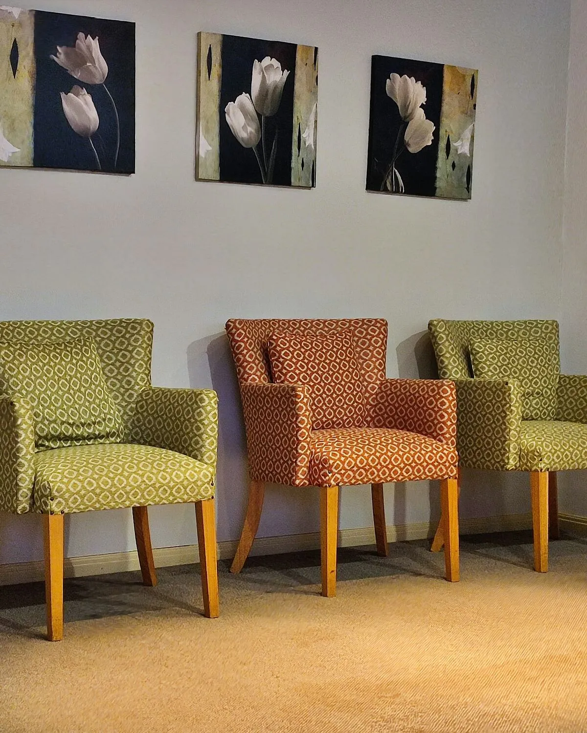 Patterned armchairs in the waiting room under three flower prints