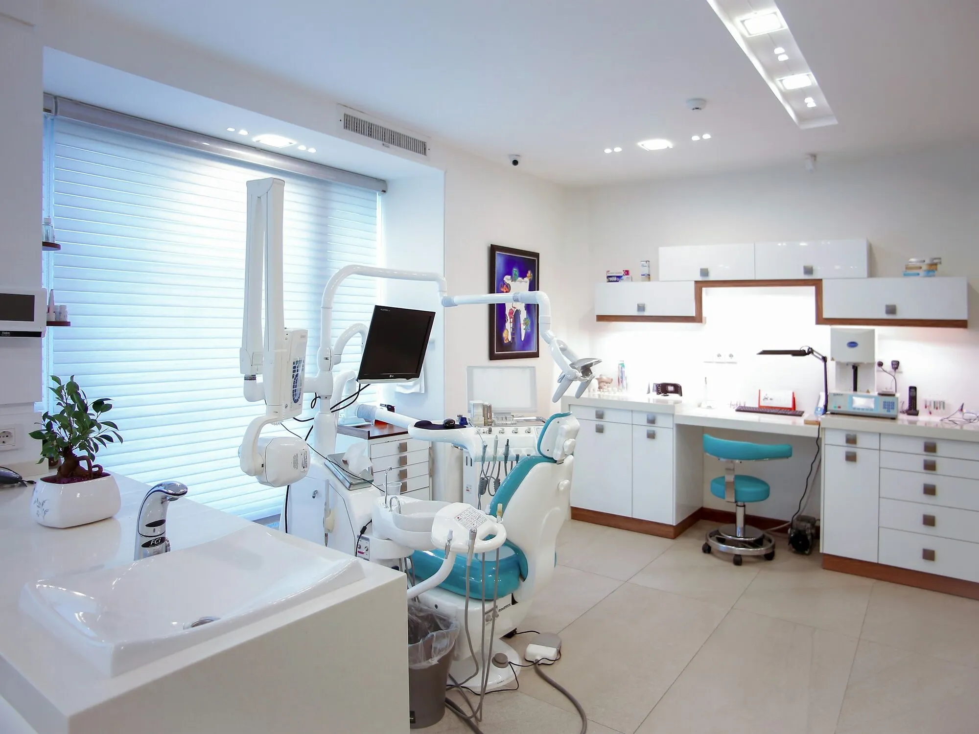 Bright treatment room with a dental chair, overhead light and a window with blinds